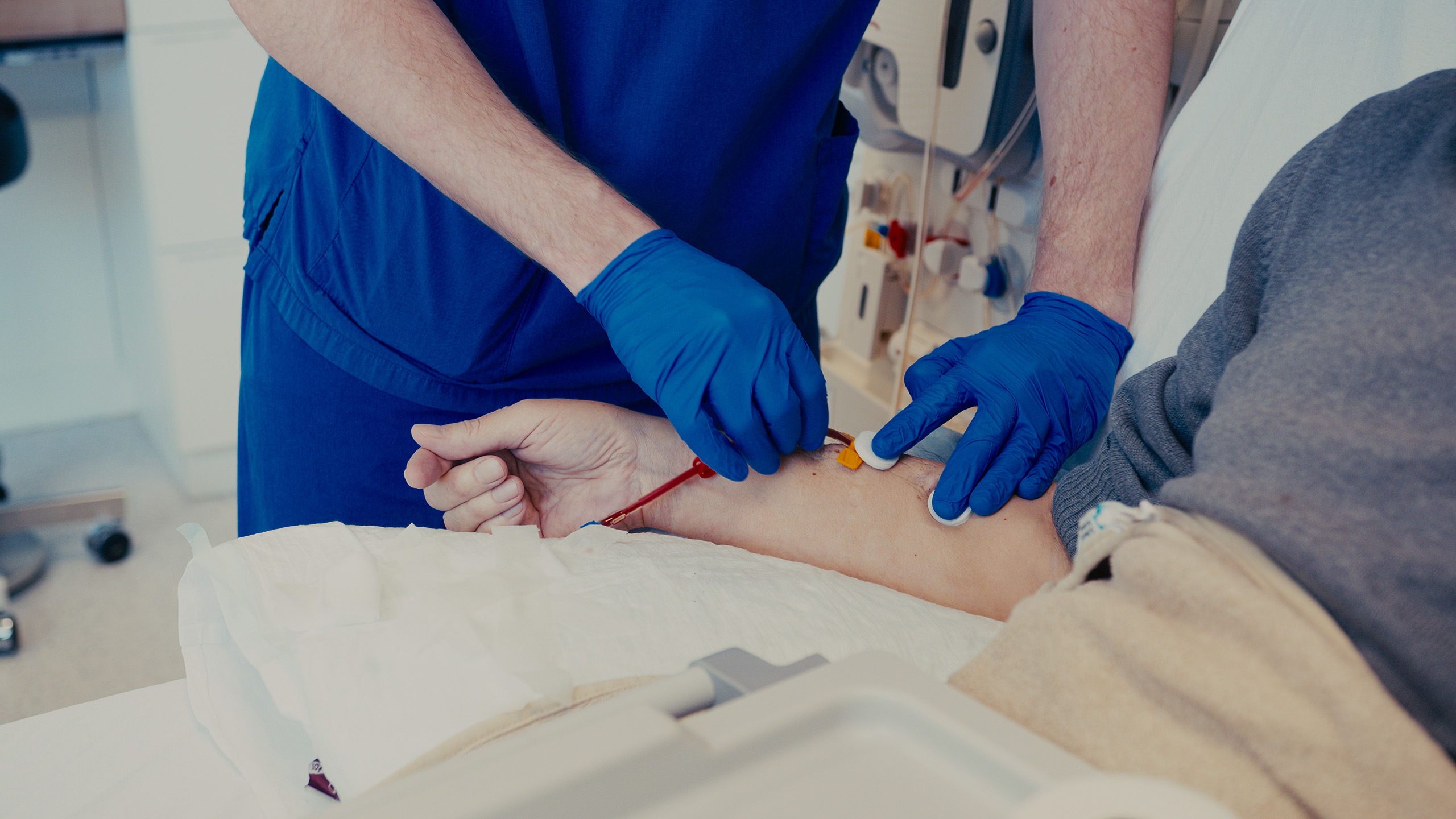 Eine medizinische Pflegefachkraft mit blauen Handschuhen bereitet den Arm eines Patienten für eine Dialysebehandlung vor.